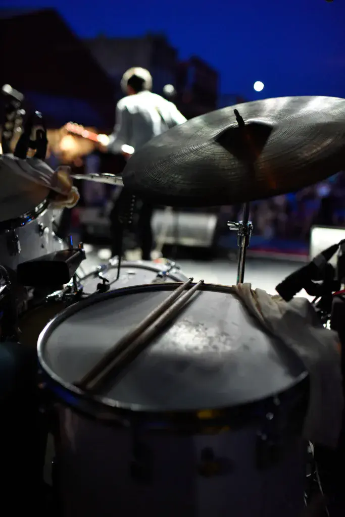 Close-up view of a drum kit with cymbals on stage during an evening performance at a music festival.