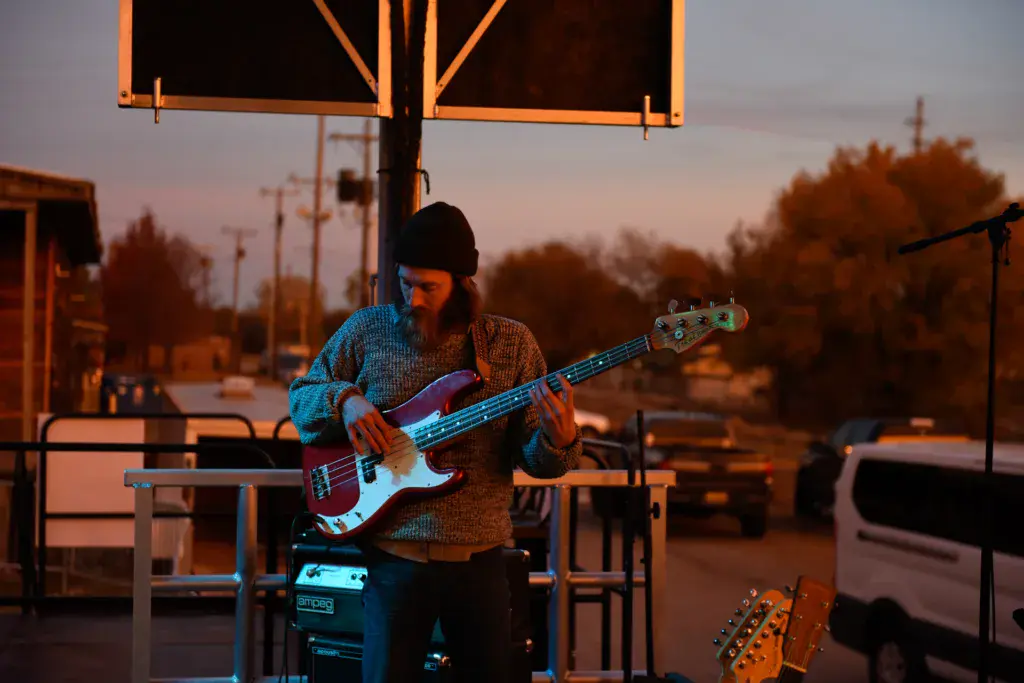 A bass guitarist performs on stage during golden hour at an outdoor music festival.