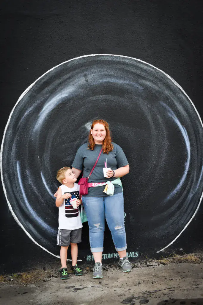 A woman and young child stand together smiling in front of a large painted tire circle at the festival.