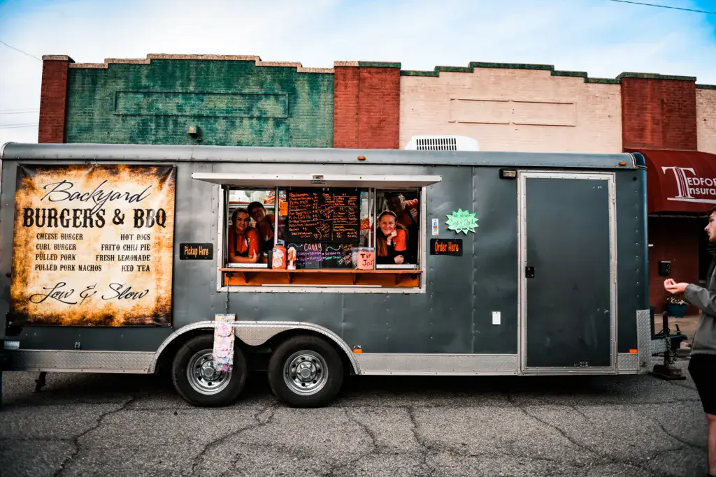 A food truck serving burgers and BBQ at the festival with staff visible inside the service window and brick buildings behind.