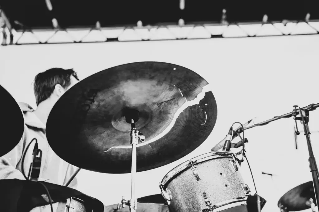 A drummer performs on stage, captured in black and white with focus on crashing cymbals and drum kit.