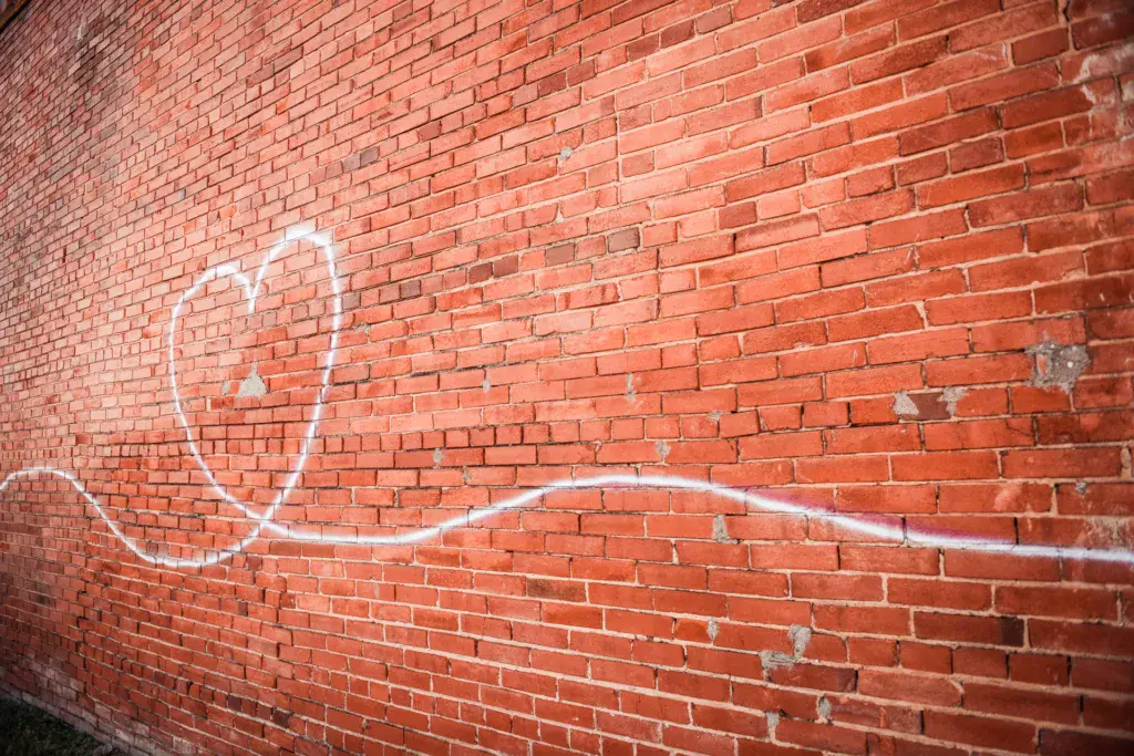 A simple smiley face drawn in white chalk on a red brick wall.
