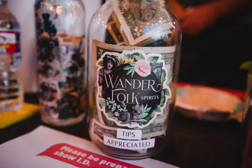 A bottle of Wander Folk Spirits with a decorative floral label sits on a table at the festival.