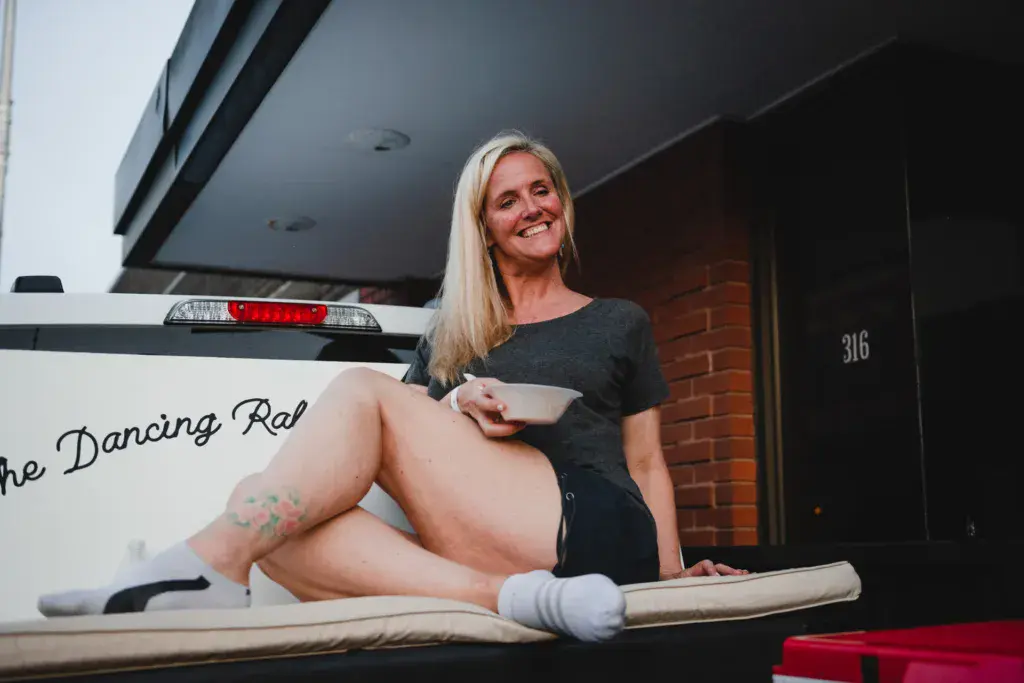 A person sits on a vehicle branded with Dancing Rabbit festival signage while holding food and smiling at the camera.
