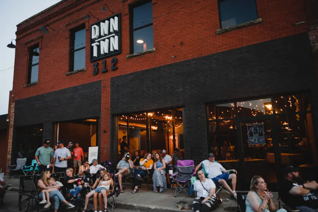 Festival crowd seated outside a brick building with illuminated windows and signage reading ONN INN.