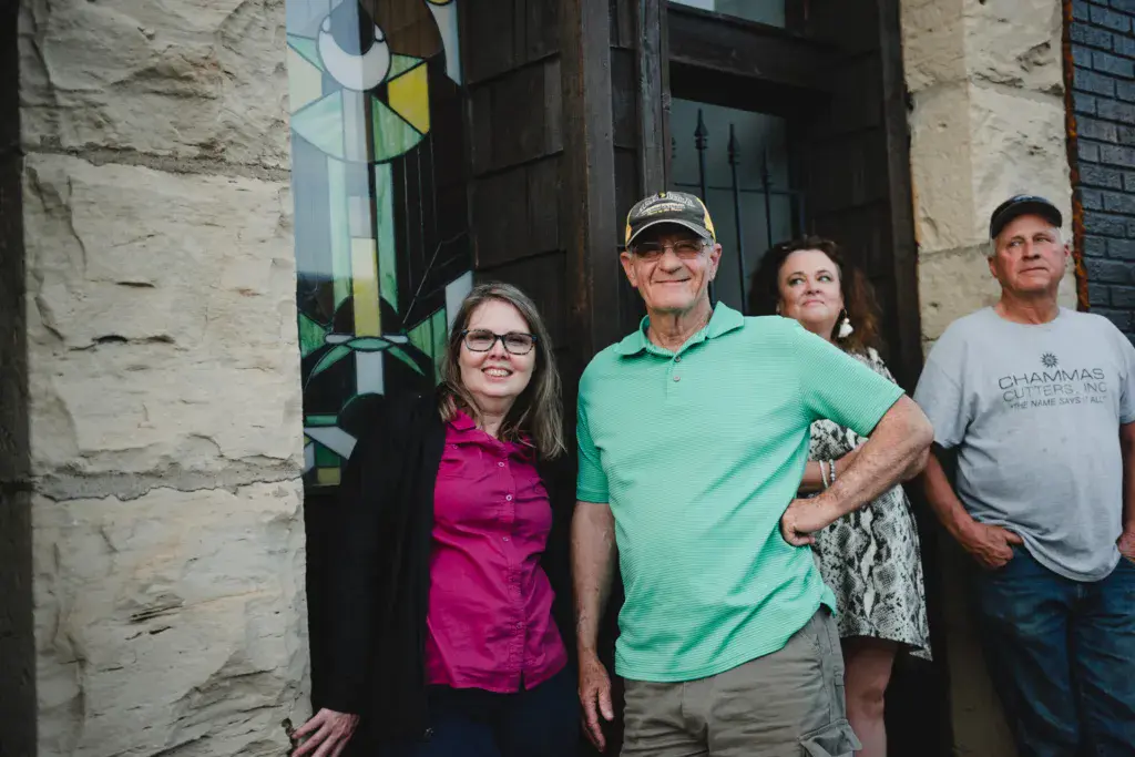 Five festival attendees pose together in front of a stone building with stained glass window.