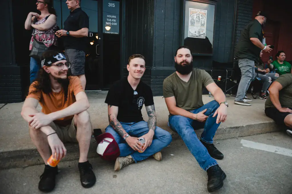 Festival attendees sit casually on the pavement outside a venue building.
