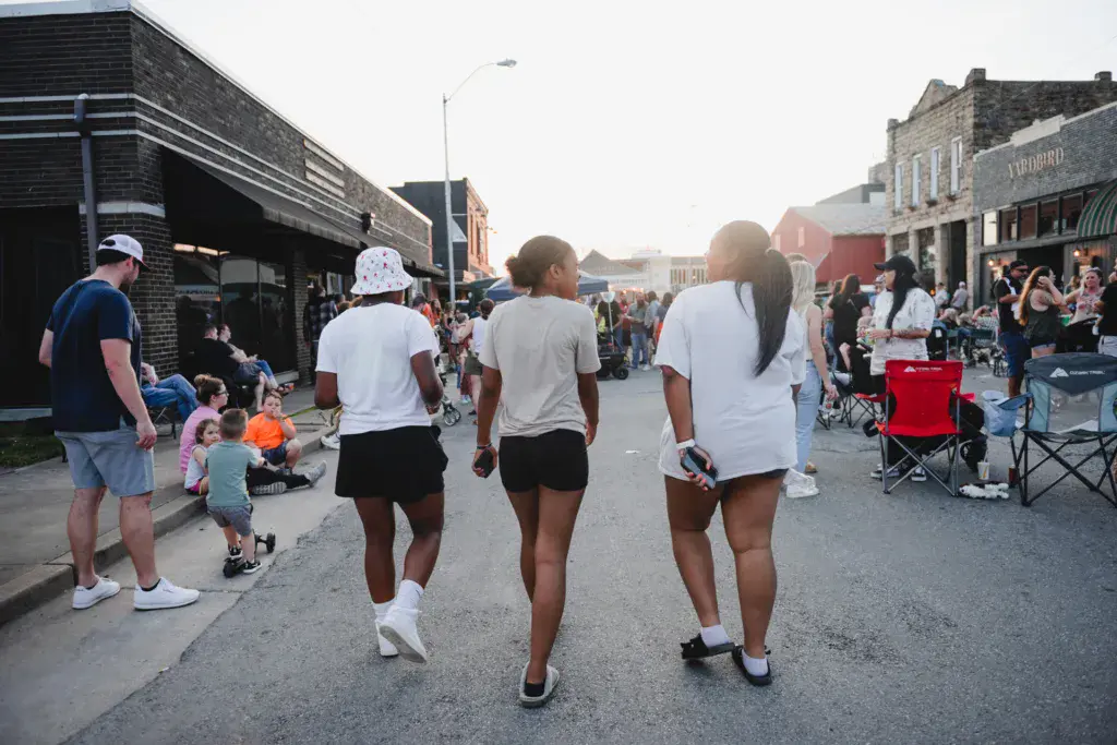 Festival-goers and families enjoy a street lined with historic brick buildings during an outdoor music event.