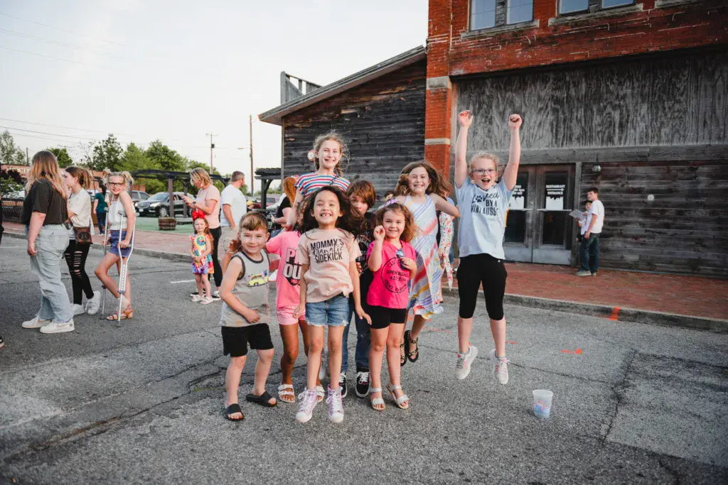 A group of children and families enjoying themselves at an outdoor festival near a historic brick building.