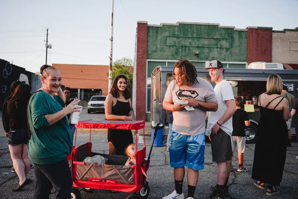 Festival attendees socialize and enjoy beverages in a parking lot venue with historic buildings in the background.