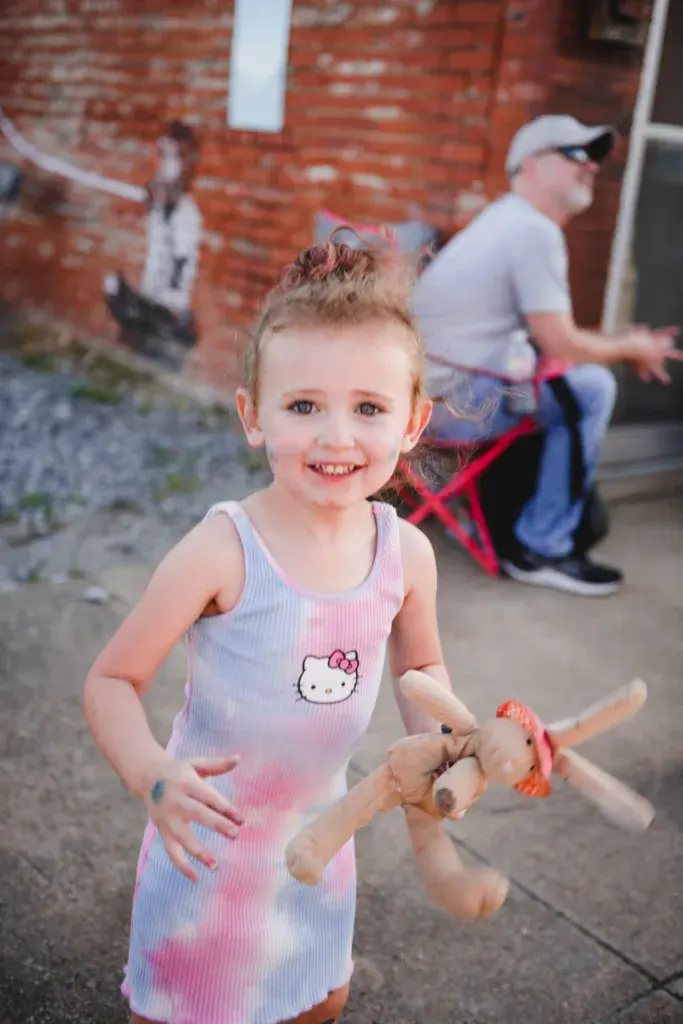 A young child smiles at the camera while holding a toy at the Dancing Rabbit Music Festival.