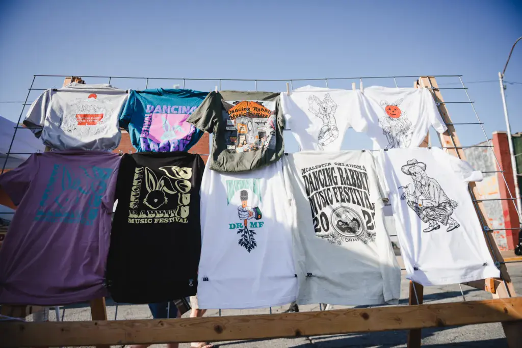 Festival merchandise t-shirts hanging on a clothesline against a clear blue sky.