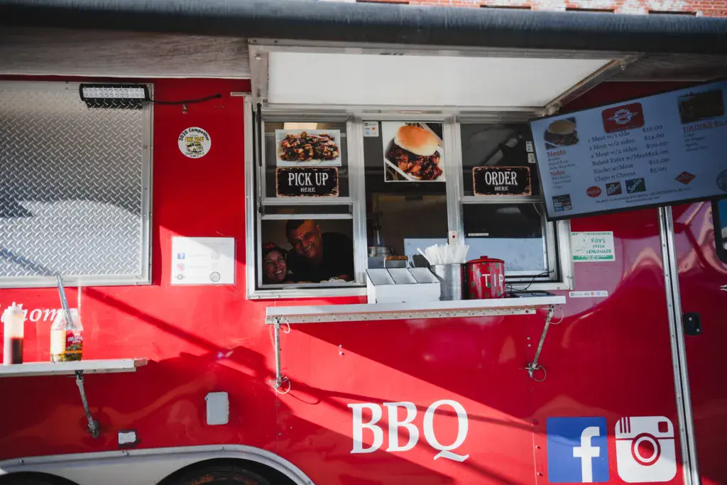 A bright red food truck with BBQ signage and menu boards displayed on its serving window.