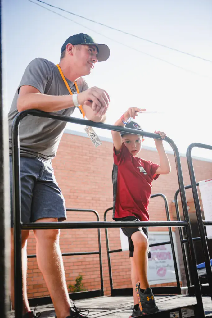 An adult and child stand together on a raised platform against a brick wall backdrop at the festival.