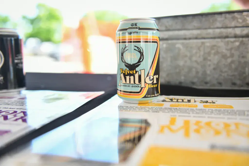 A can of Velvet Antler beer sits on a table at an outdoor music festival with promotional materials nearby.