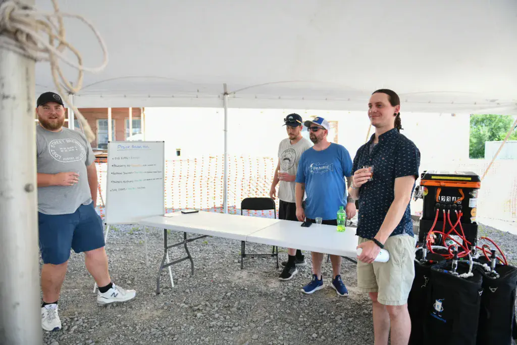 Festival organizers and volunteers stand beneath a tent structure at an outdoor event booth.