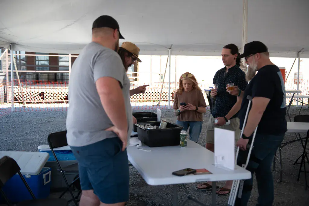 Festivalgoers gather around a white table under a tent at an outdoor event