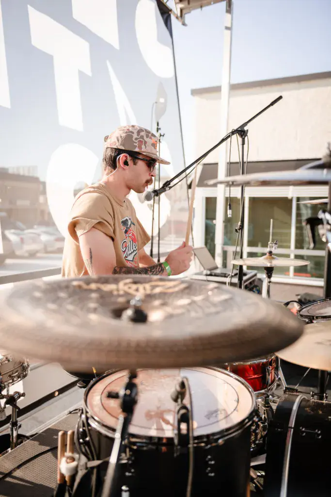 Drummer performs at an outdoor venue with drums in sharp focus in the foreground.
