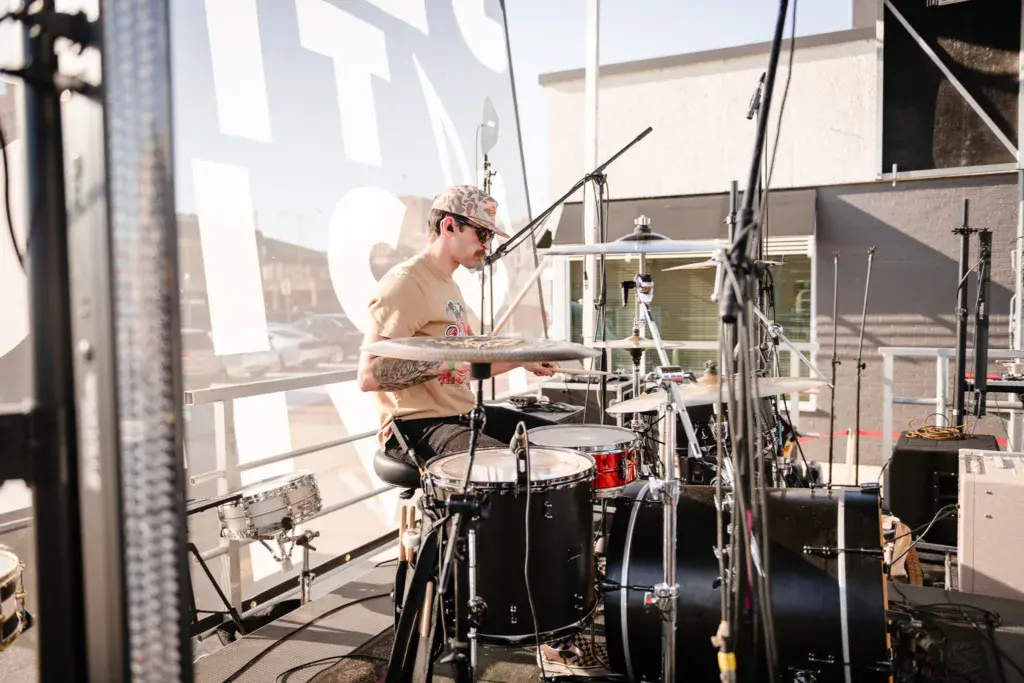 Drummer performing at an outdoor festival stage setup on a rooftop venue during daytime.