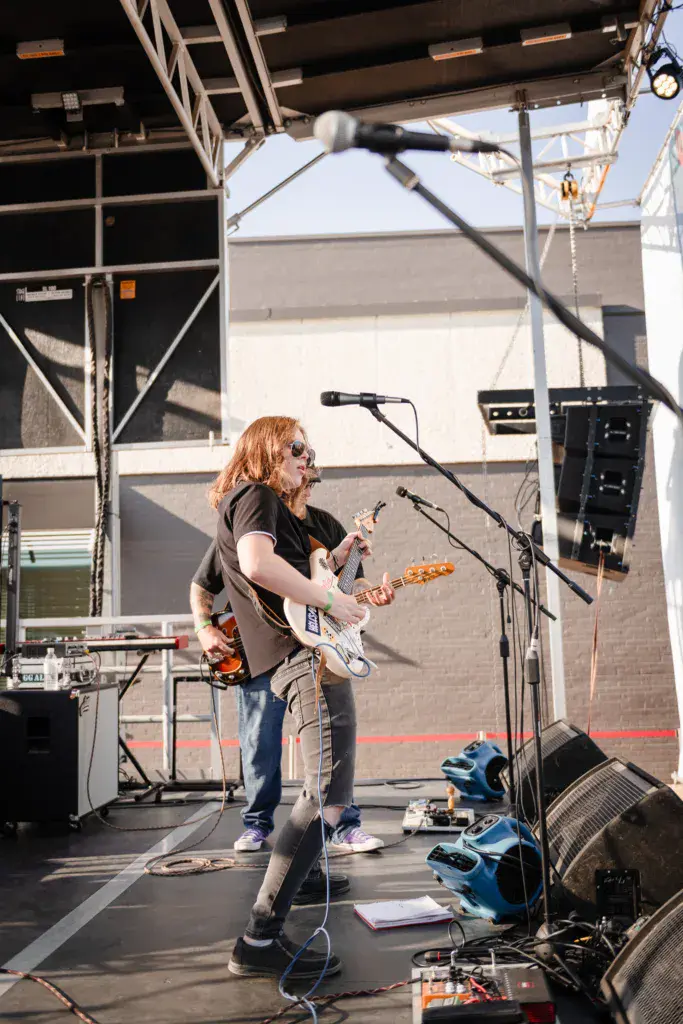 Guitarist with long reddish hair performs on stage under professional lighting and equipment.