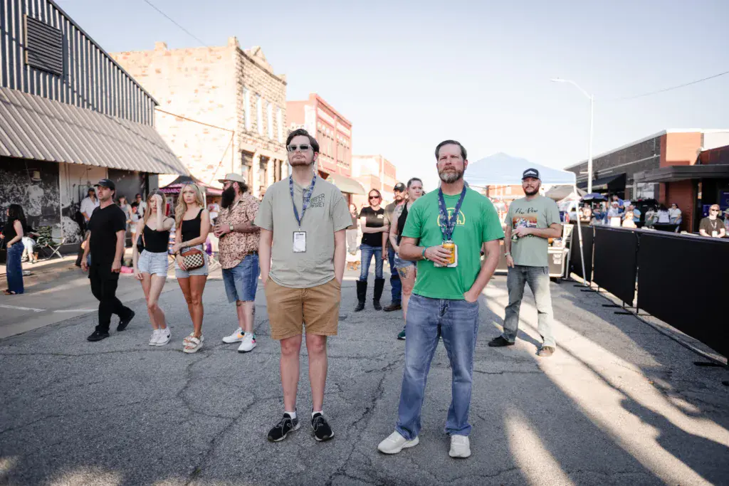Festival attendees walk through an outdoor venue street with historic brick buildings in the background.