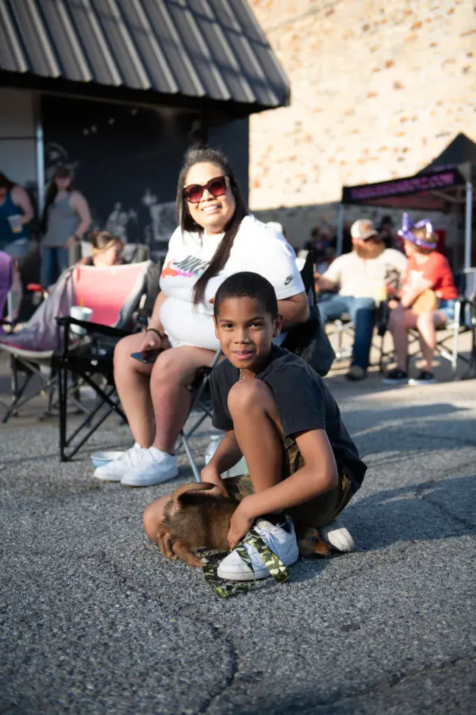 A woman and young child pose together at an outdoor festival venue on a sunny day.