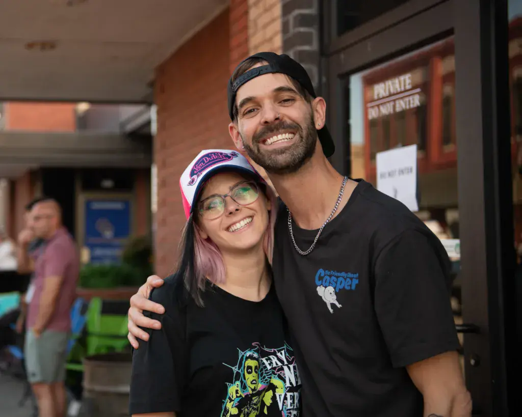 Two smiling festival attendees posing together outside a brick venue building.