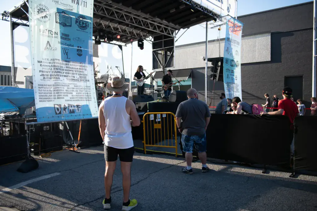 Festival attendees watch a band perform on an outdoor stage with sponsor signage visible.