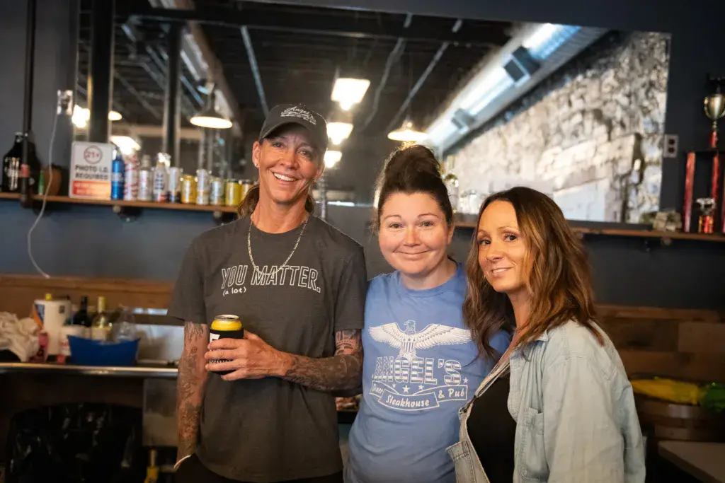 Three people smiling together inside a bar or food vendor area at the festival.