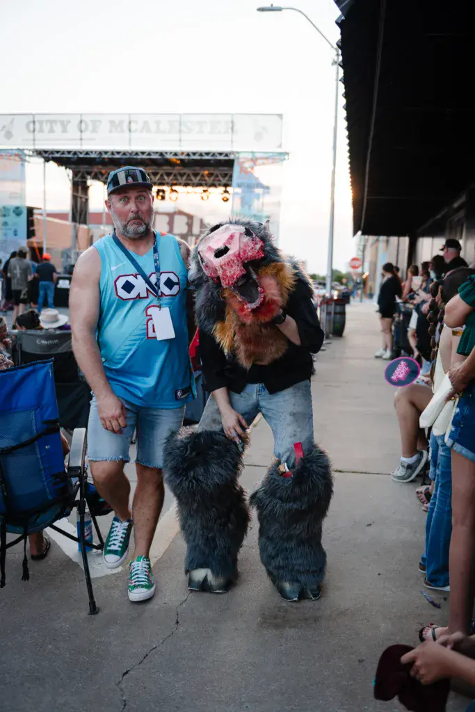 Festival attendees in creative costumes pose together on the grounds near the stage.
