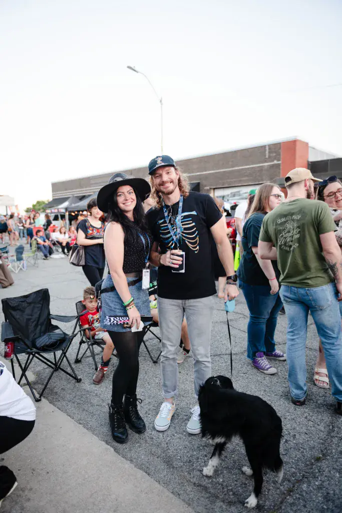 Two festivalgoers in creative costumes pose together at Dancing Rabbit Music Festival with a dog and crowd nearby.