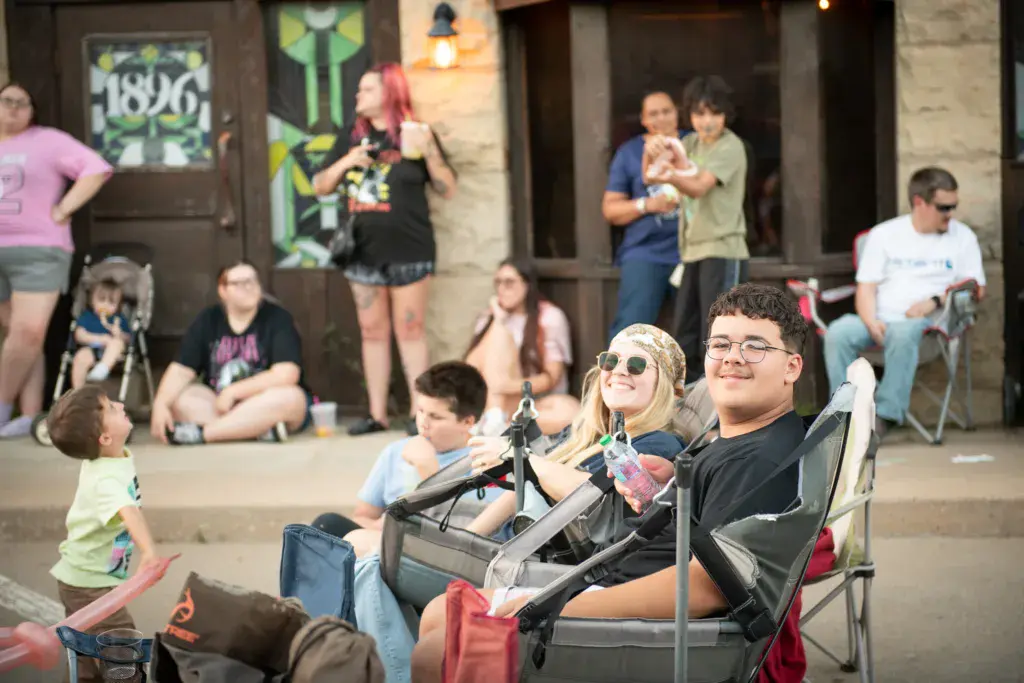 Festival attendees sit in lawn chairs watching performers, with a crowd gathered in an outdoor venue.