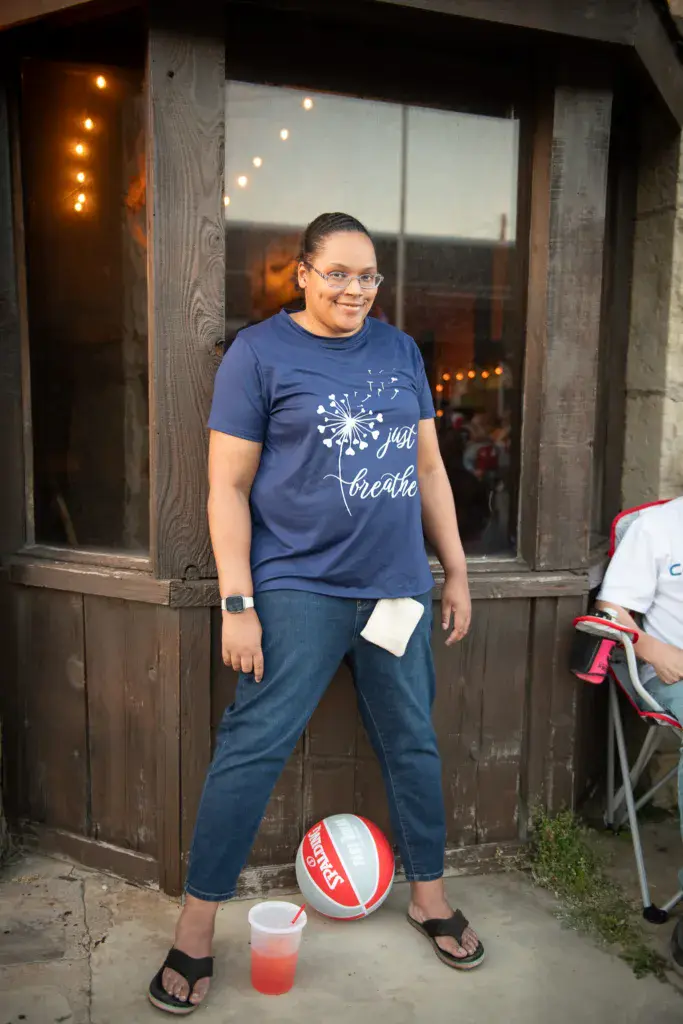 Person in blue graphic tee posing in front of wooden venue doors with warm lighting.
