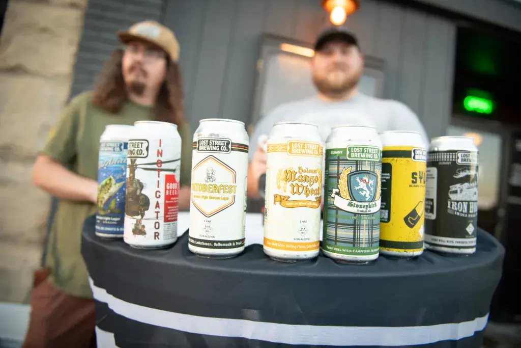 A display table showcases various craft beer cans with two people standing behind it at an indoor venue.