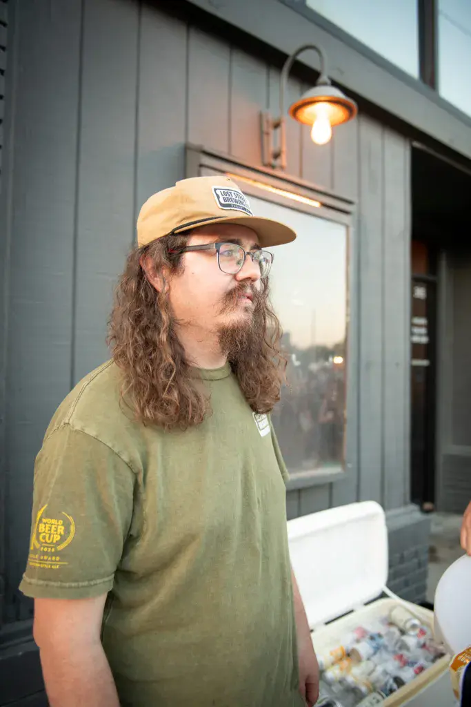 Person wearing a tan cap and olive green shirt stands outside a venue building at dusk.