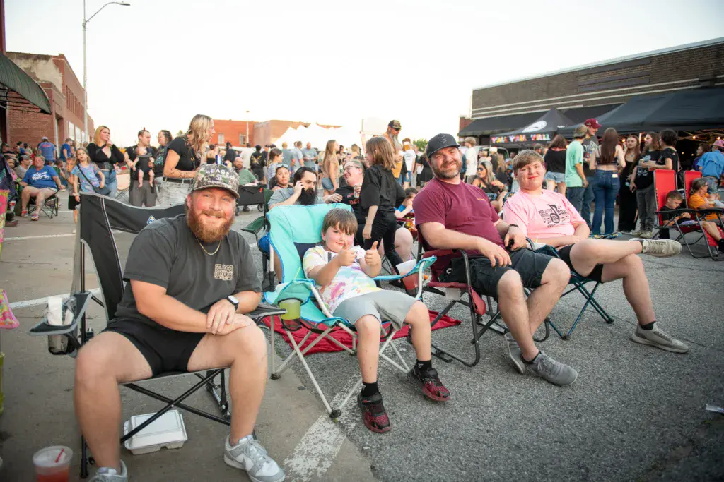 Festivalgoers sit in folding chairs on an outdoor street watching performances at Dancing Rabbit Music Festival.