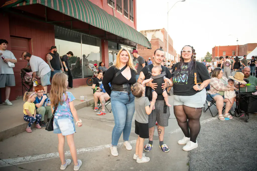 Adults and children dancing and moving together on an outdoor festival street lined with brick buildings.