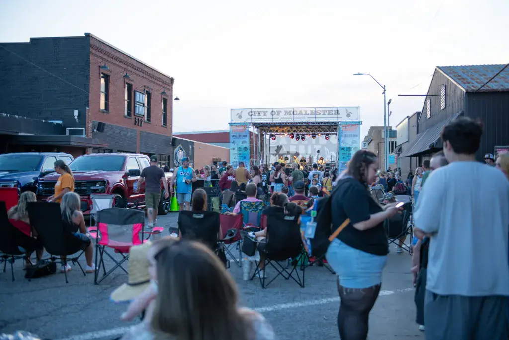 A crowd gathers in an outdoor city venue for the Dancing Rabbit Music Festival, with a decorated stage in the background.
