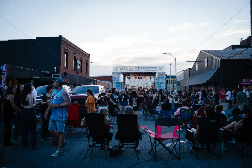Outdoor music festival crowd gathered in front of an illuminated stage in an urban venue during evening hours.
