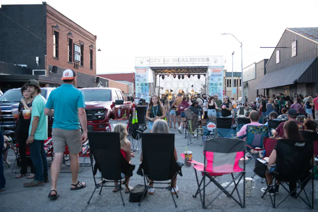 Outdoor music festival crowd gathered in an urban parking area with stage and industrial buildings in background