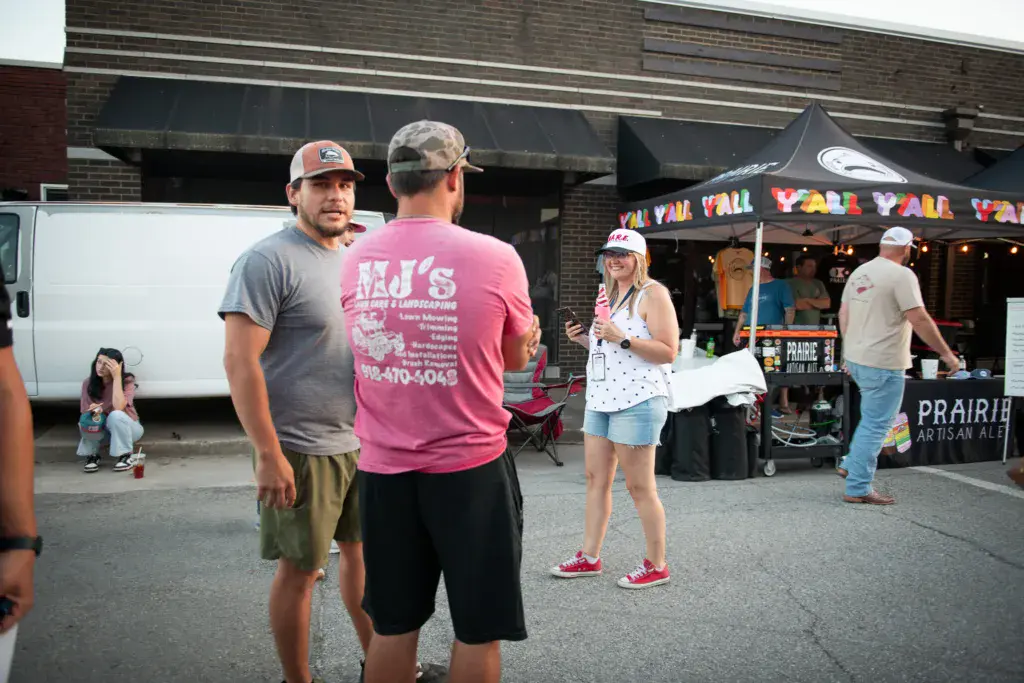 Festival attendees and vendors interact in an outdoor venue area with tents and signage visible.