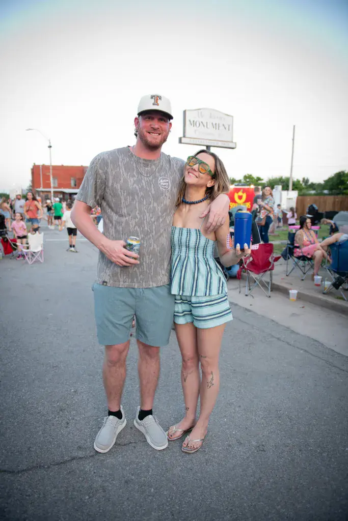 Two festival attendees posing together outdoors with crowds and signage visible in the background.