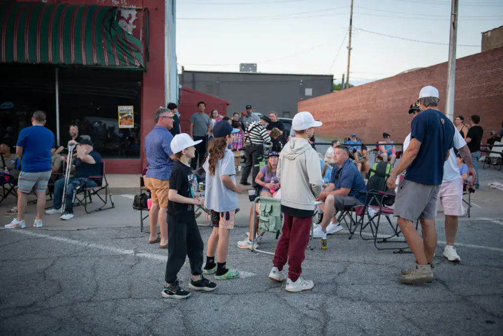 Festival attendees gather in a brick courtyard with camping chairs and instruments during daytime at Dancing Rabbit Music Festival.