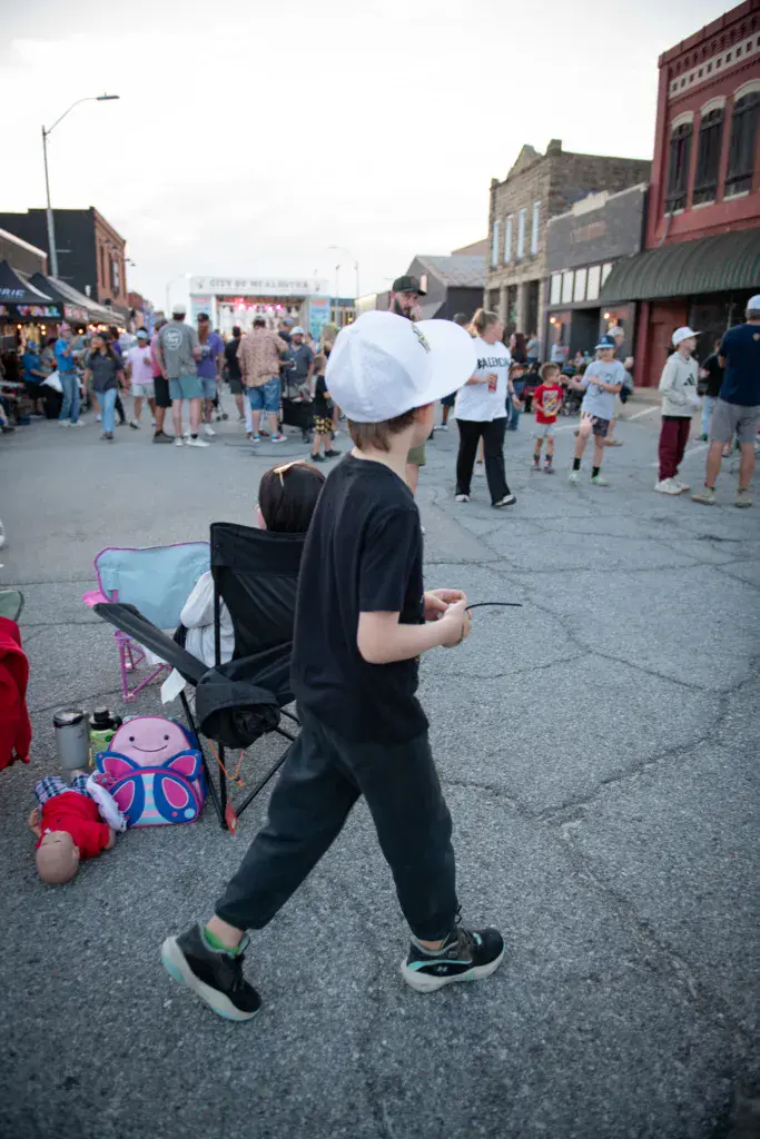 A young child in a white cap and black outfit runs through a crowded festival street lined with historic brick buildings.