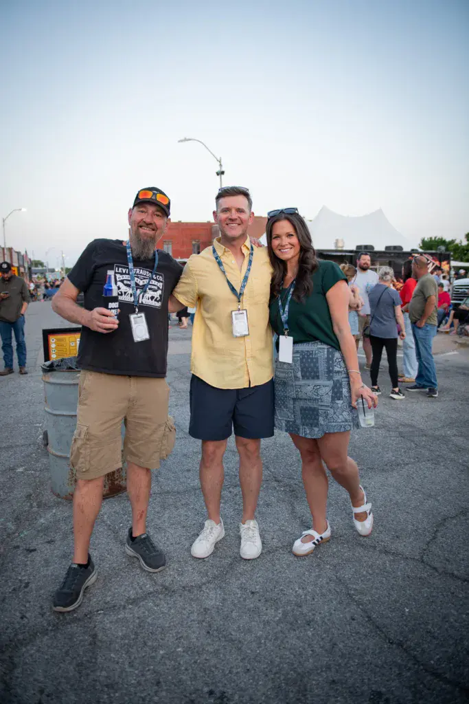 Three festival attendees wearing credential badges pose together at the Dancing Rabbit Music Festival venue.