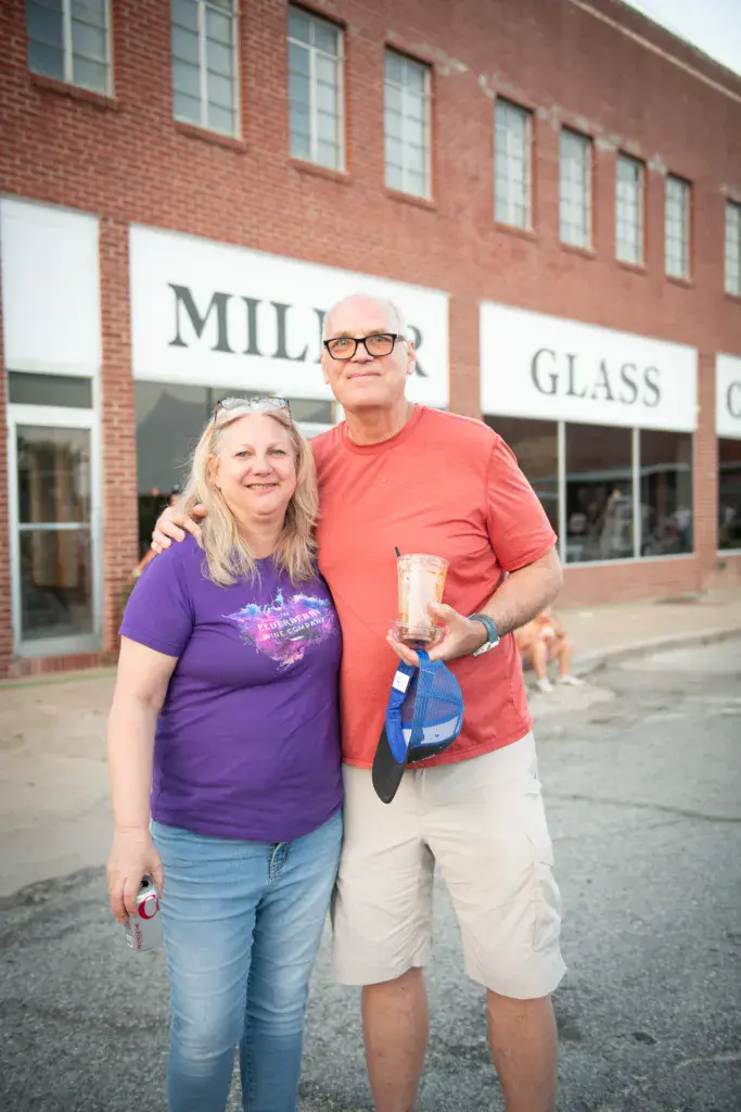Two festival attendees smile together holding drinks in front of a brick building