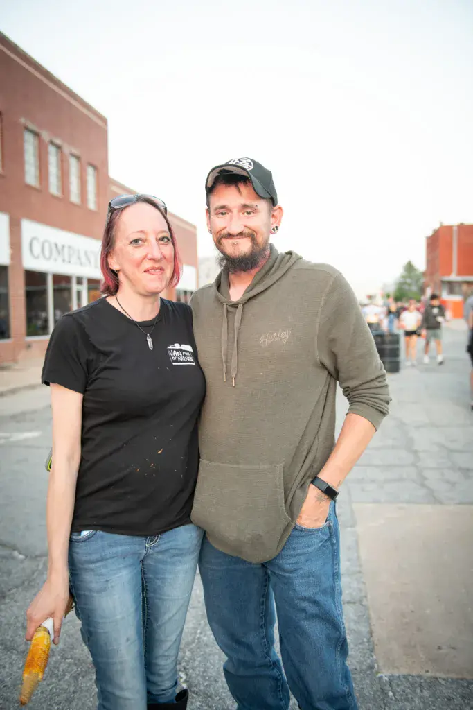 Two attendees pose together on a street at Dancing Rabbit Music Festival with brick buildings in the background.