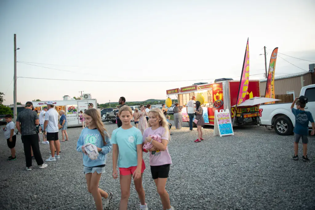 Young attendees walk through a festival vendor area with food trucks and colorful festival stands.