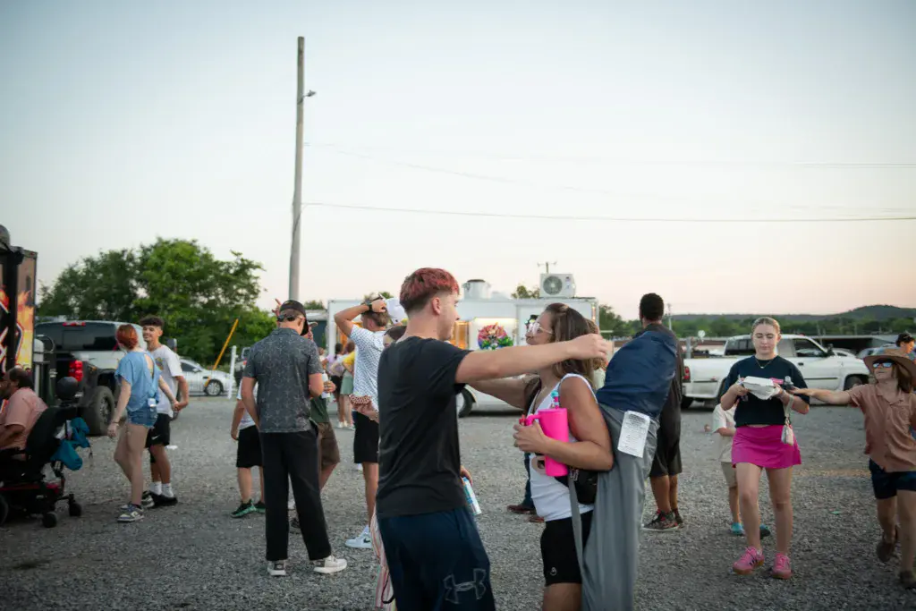 Festival attendees gathered in a parking lot during evening hours, socializing and dancing under dimming sky.