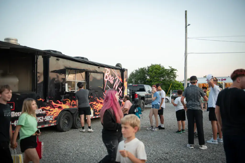 Festival attendees gather around a food truck with flame graphics at an outdoor event.